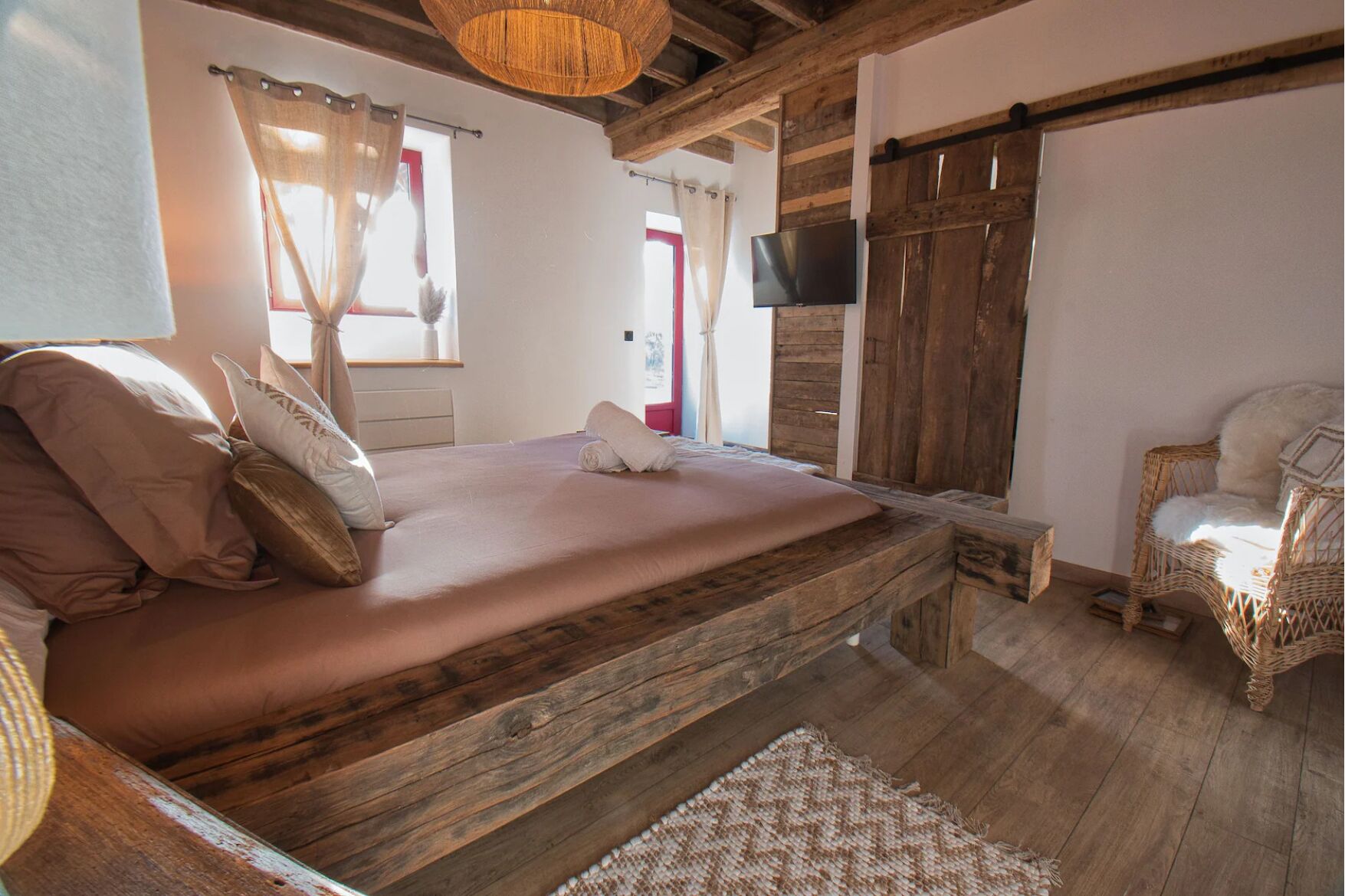 A rustic bedroom with a wooden bed, a television, and a wicker chair.