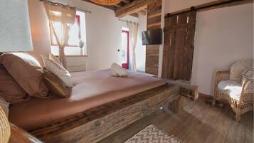 A rustic bedroom with a wooden bed, a television, and a wicker chair.