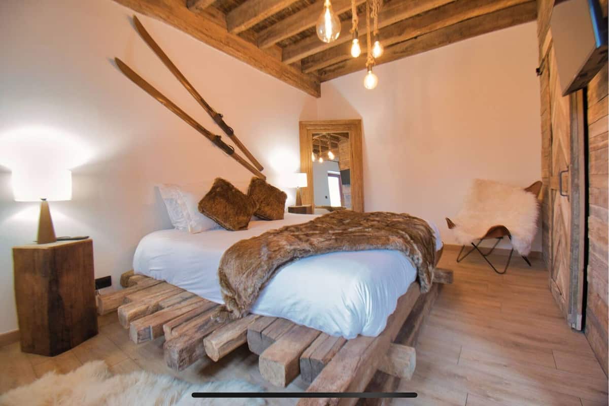 A rustic bedroom with a wooden bed frame, a mirror, and a chair.
