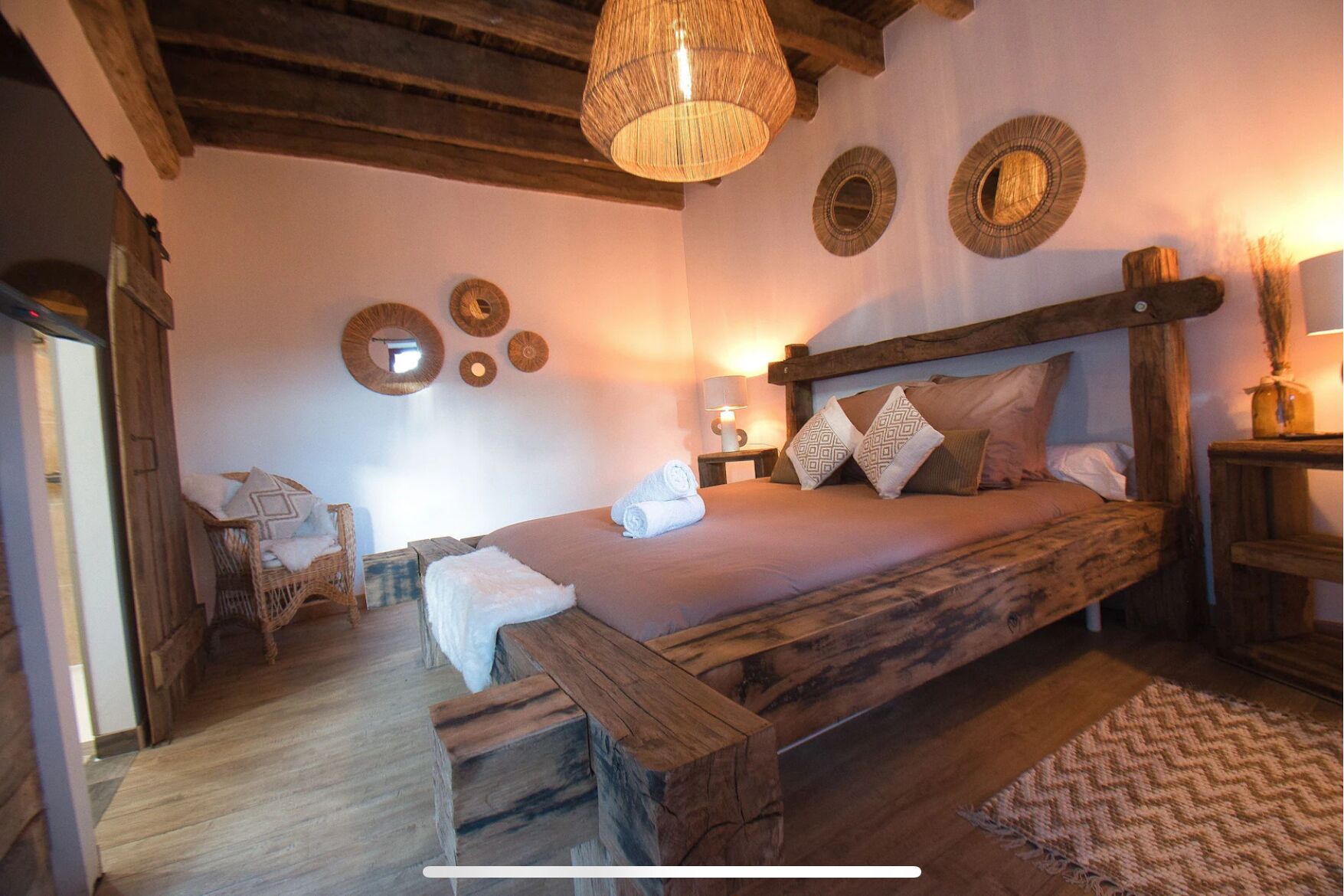 A rustic bedroom with a wooden bed, a woven light fixture, and wall decor.
