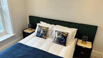 A neatly made bed with white linens and a blue quilt, flanked by two bedside tables with lamps and decorative pillows.