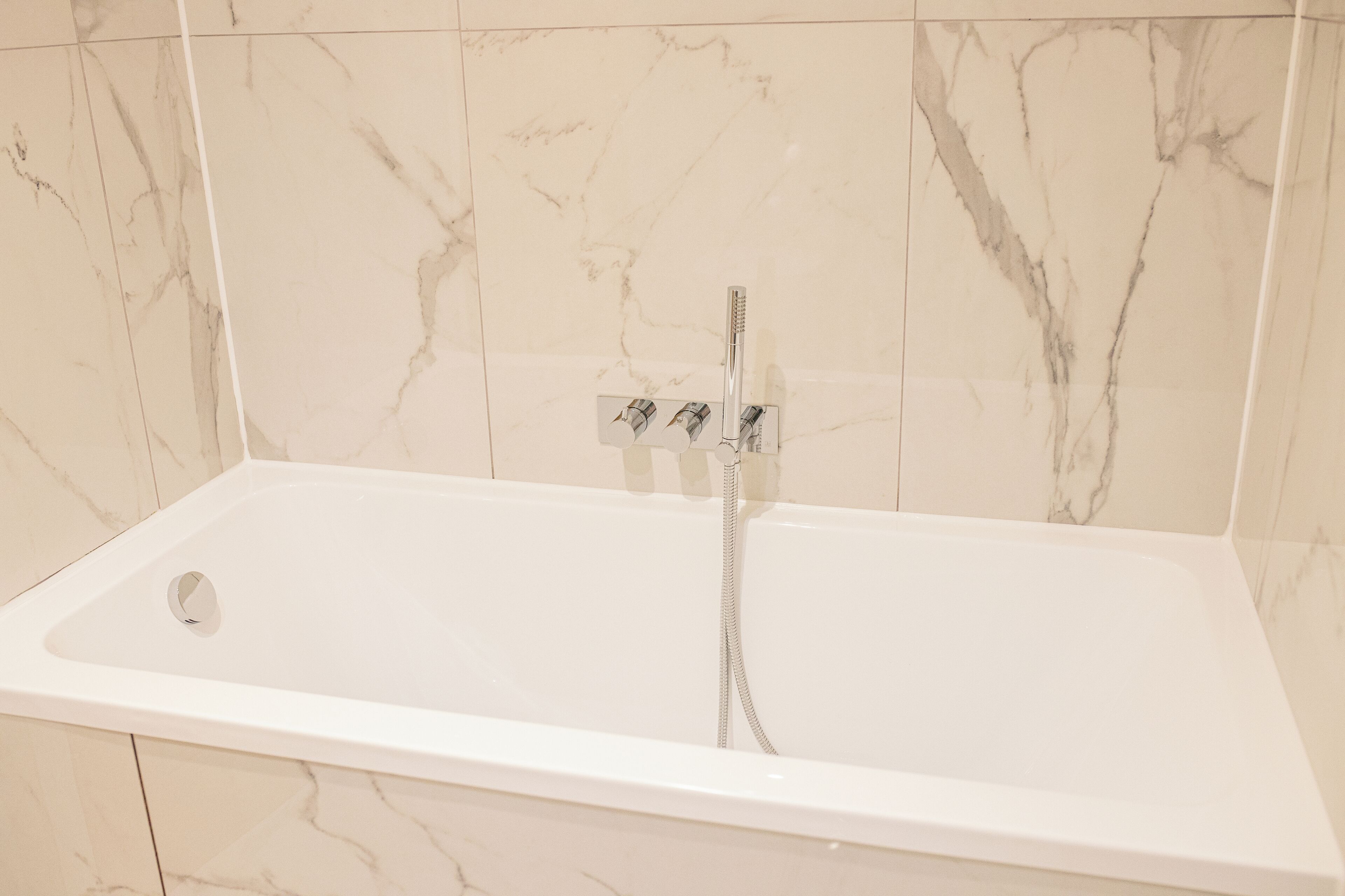 A bathroom with a white bathtub, a showerhead, and a control panel.