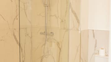 Eine begehbare Dusche mit Glaswänden, einer Handbrause und einem am Wand befestigten Wasserhahn.