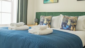 A neatly made bed with blue bedding and white pillows, a green headboard, and artwork on the walls. - Charles Hope Salisbury Centre (Salisbury)