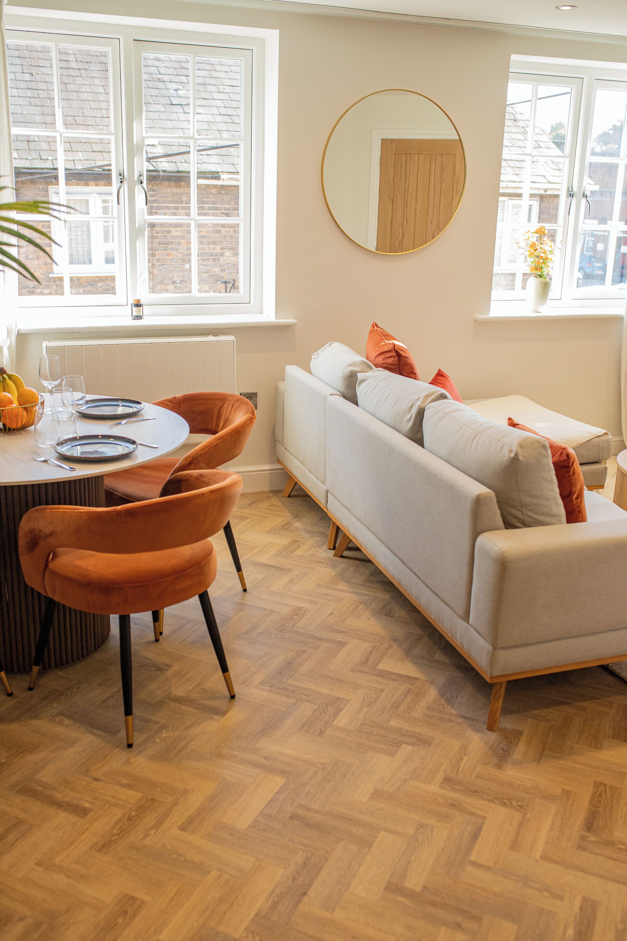 Un coin repas avec une table ronde, des chaises orange et un canapé blanc.