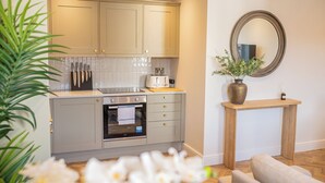 A modern kitchen with light-colored cabinets, a built-in oven, and a wooden console table with a vase and mirror. - Charles Hope Salisbury Centre (Salisbury)