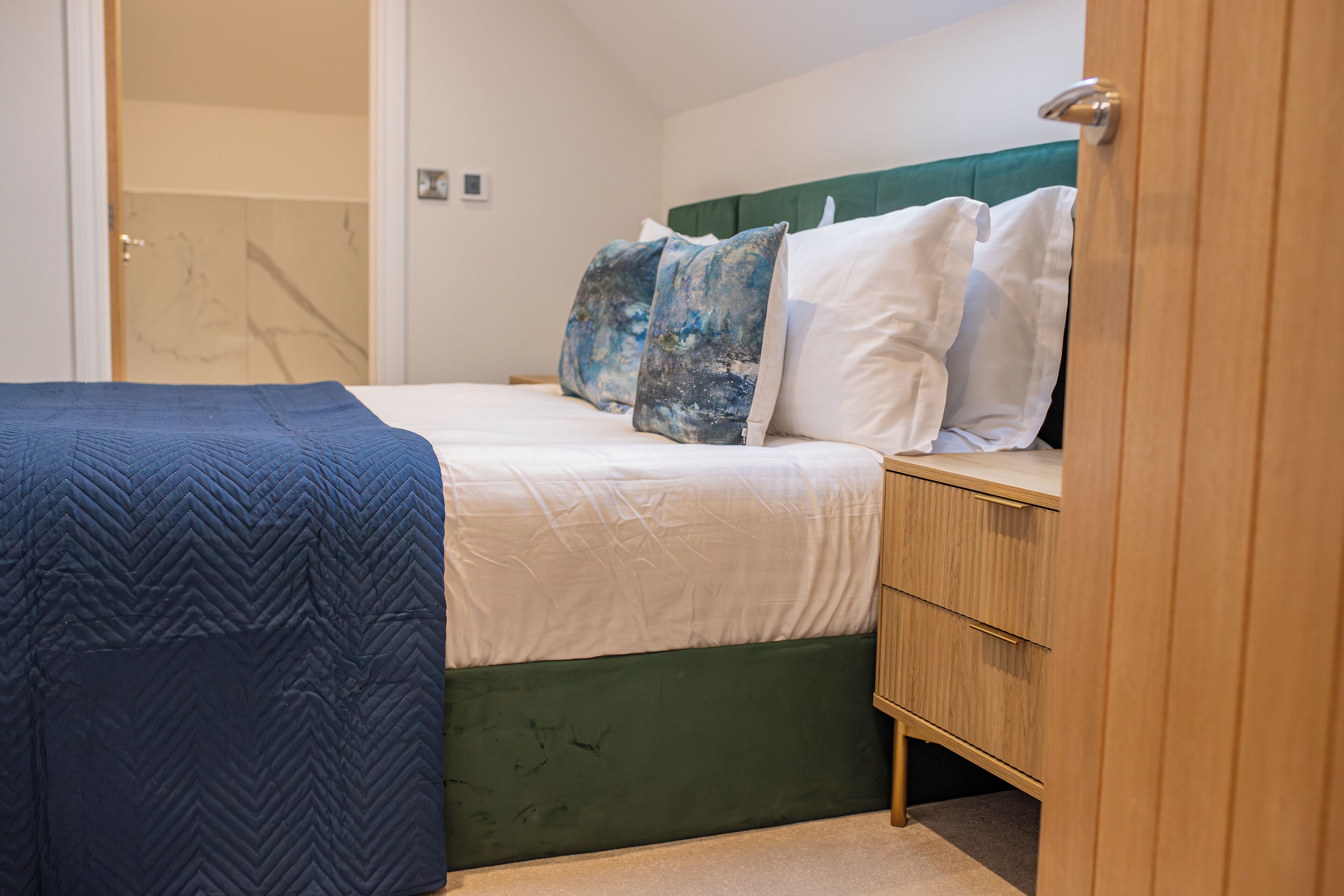A bedroom with a bed, a wooden nightstand, and a green upholstered headboard.
