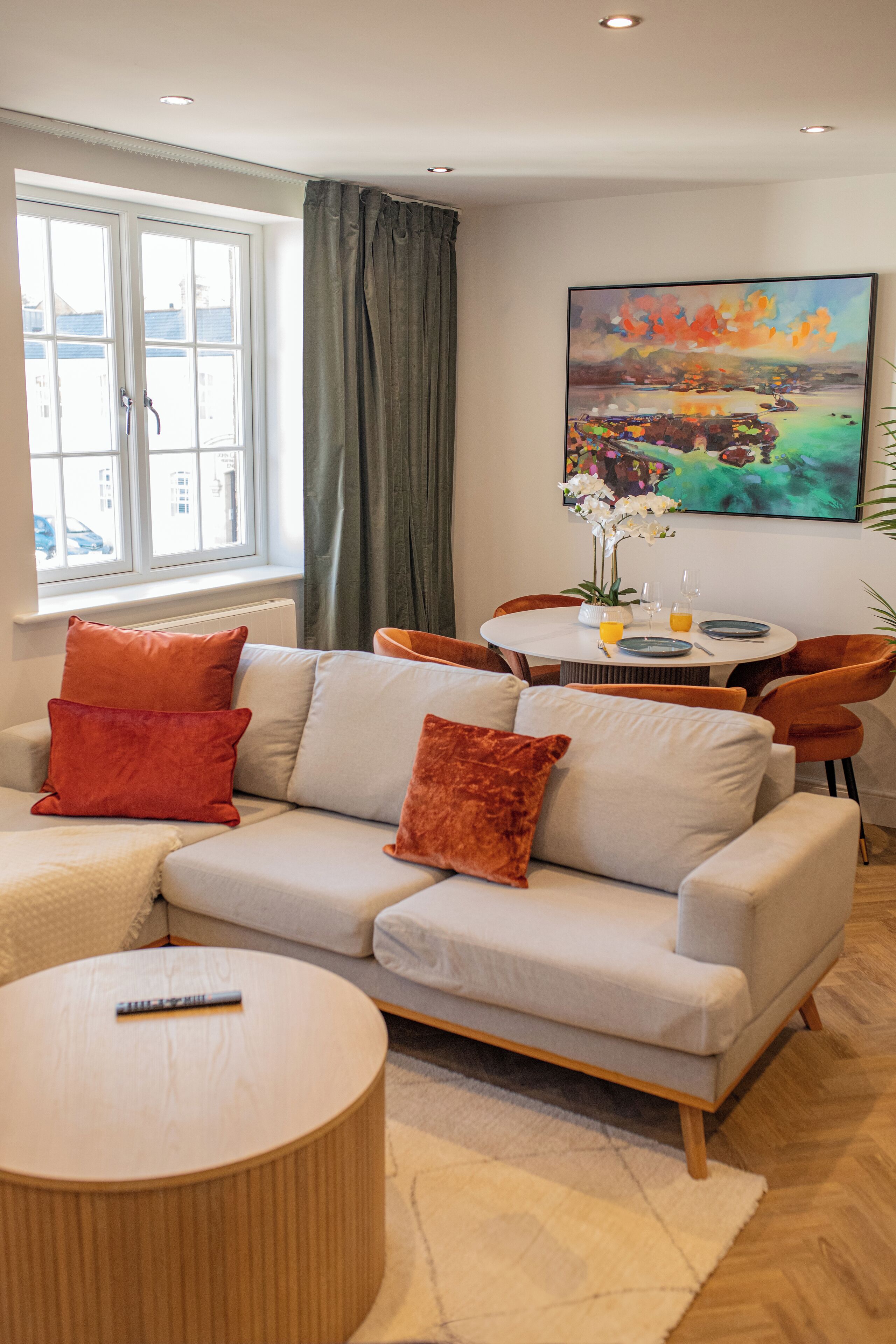 A modern living room with a sofa, a round coffee table, and a dining table set for two.
