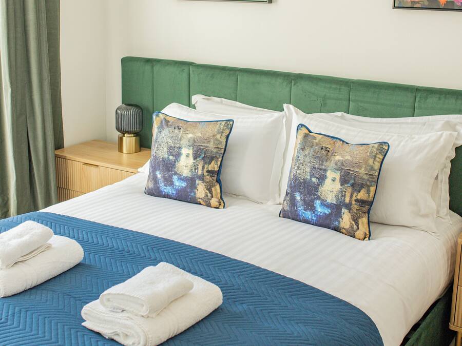 Una cama bien hecha con un edredón azul, dos almohadas con diseños abstractos y un cabecero verde.