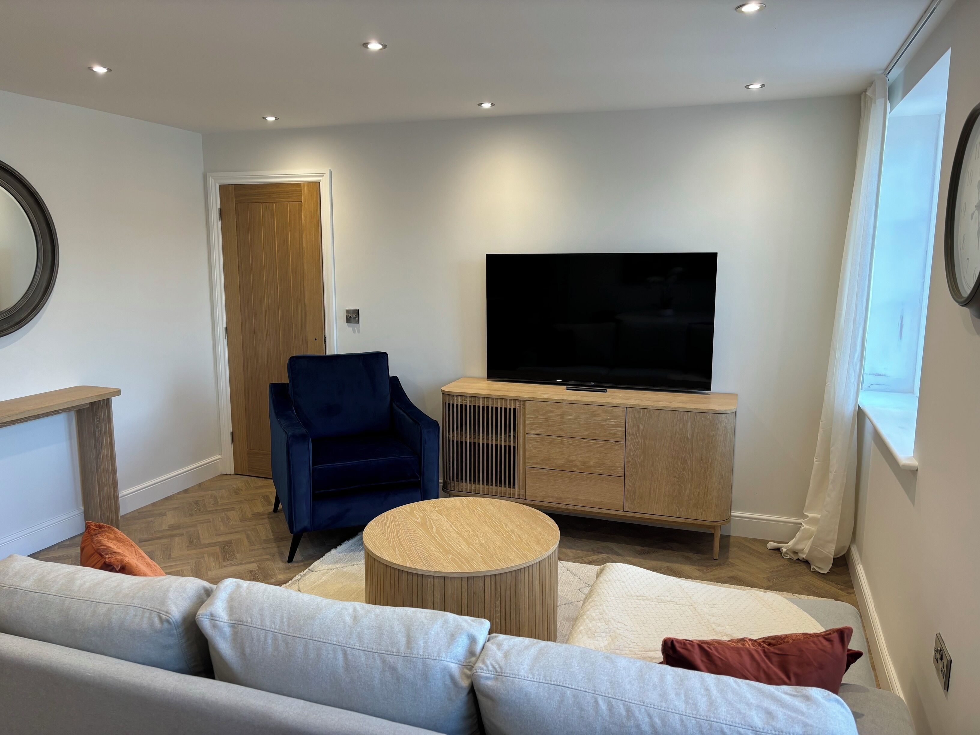 Ein modernes Wohnzimmer mit einer Couch, einem blauen Sessel, einem Fernseher auf einer Holzkommode und einem runden Couchtisch.