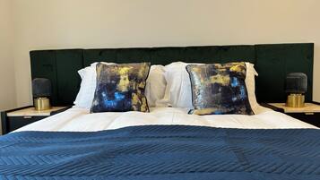 Ein Bett mit einer blauen Steude, zwei Kissen mit einem goldenen und blauen abstrakten Muster sowie zwei Nachttische mit modernem Design.