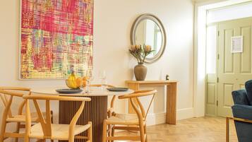Un coin repas avec une table ronde, quatre chaises en bois, un vase de fleurs et un grand tableau abstrait accroché au mur.