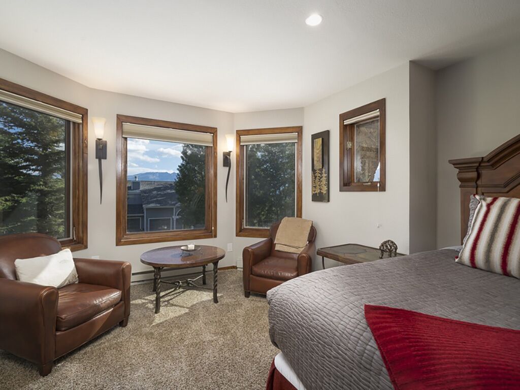 A bedroom with a large bed, a brown leather chair, a small table, and a window with a view of trees and hills.
