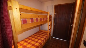 Ein kleines Zimmer mit einem Etagenbett und einem Einzelbett, einer Holztür und einem gefliesten Boden.