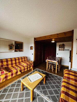 A cozy living room with a plaid sofa, a wooden coffee table, and a dining area with a wooden table and chairs.