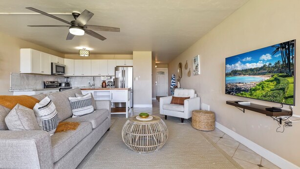 A modern living room with a grey sofa, a coffee table, and a TV mounted on the wall. - Kamaole Beach 1 Condo at Kihei Ali'i Kai (Kihei)