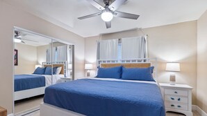 A bedroom with a large bed, two bedside tables, a ceiling fan, and a window with curtains. - Kamaole Beach 1 Condo at Kihei Ali'i Kai (Kihei)