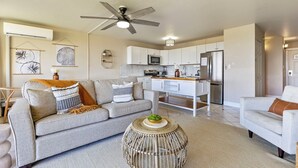 A modern living room with a grey sofa, a round woven coffee table, and a ceiling fan.