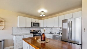 A kitchen with white cabinets, a stainless steel refrigerator, a microwave, and a wooden countertop.