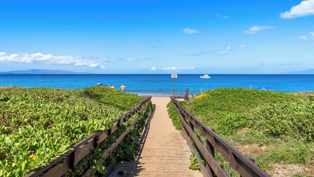 A wooden boardwalk leading to a beach with lush greenery on both sides.
