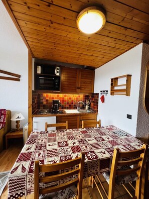 A cozy kitchen with wooden cabinets, a tiled backsplash, and a dining table set with patterned tablecloths.