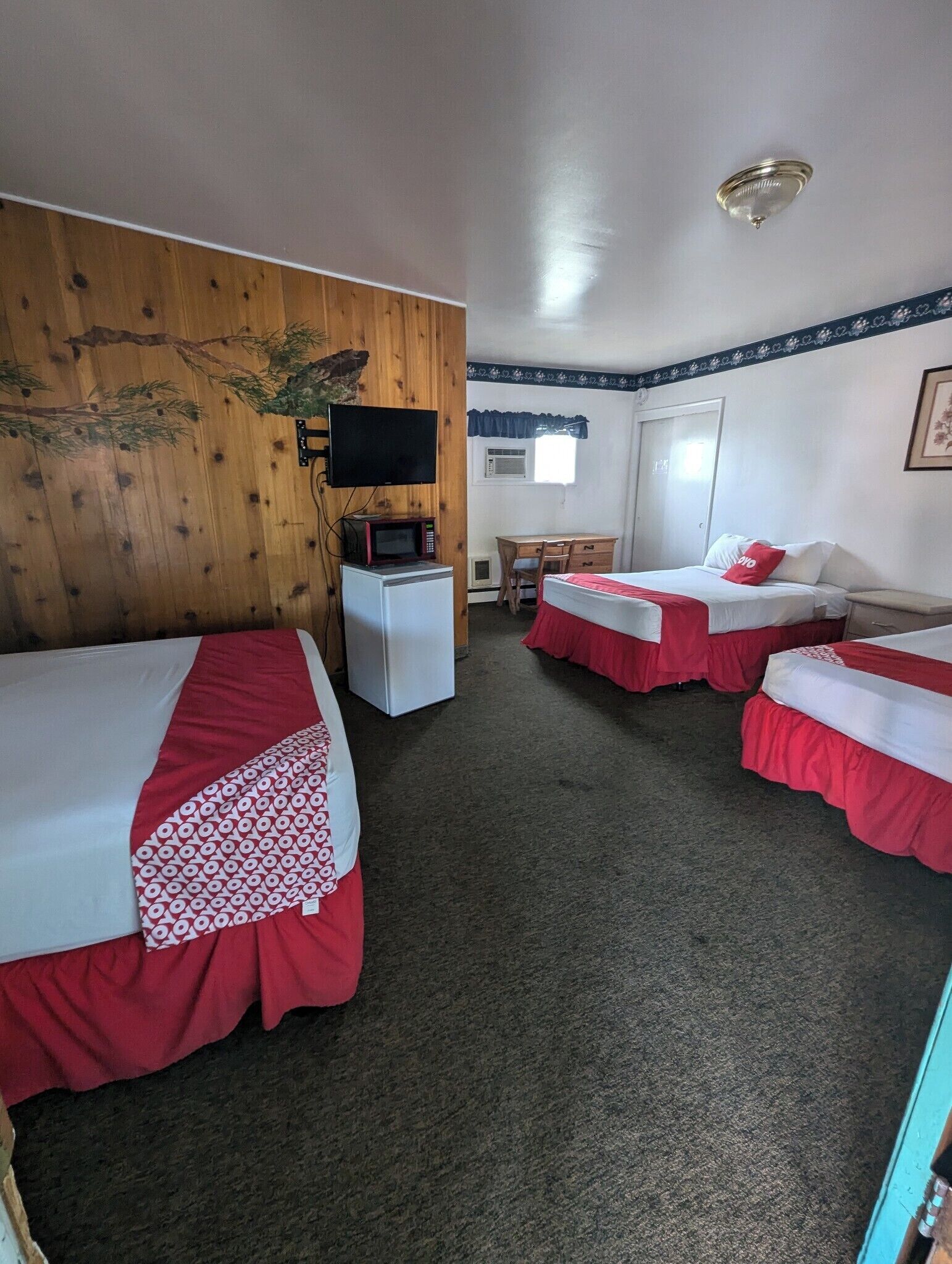 Una habitación de hotel con dos camas individuales, un escritorio con silla, televisor, microondas y refrigerador.