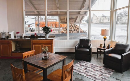 A cozy interior with a wooden table, chairs, a bar area, and large windows offering a view of the outside.