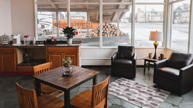 A cozy interior with a wooden table, chairs, a bar area, and large windows offering a view of the outside.