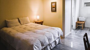 A bedroom with a bed, bedside lamp, framed picture, and a small wooden stool.
