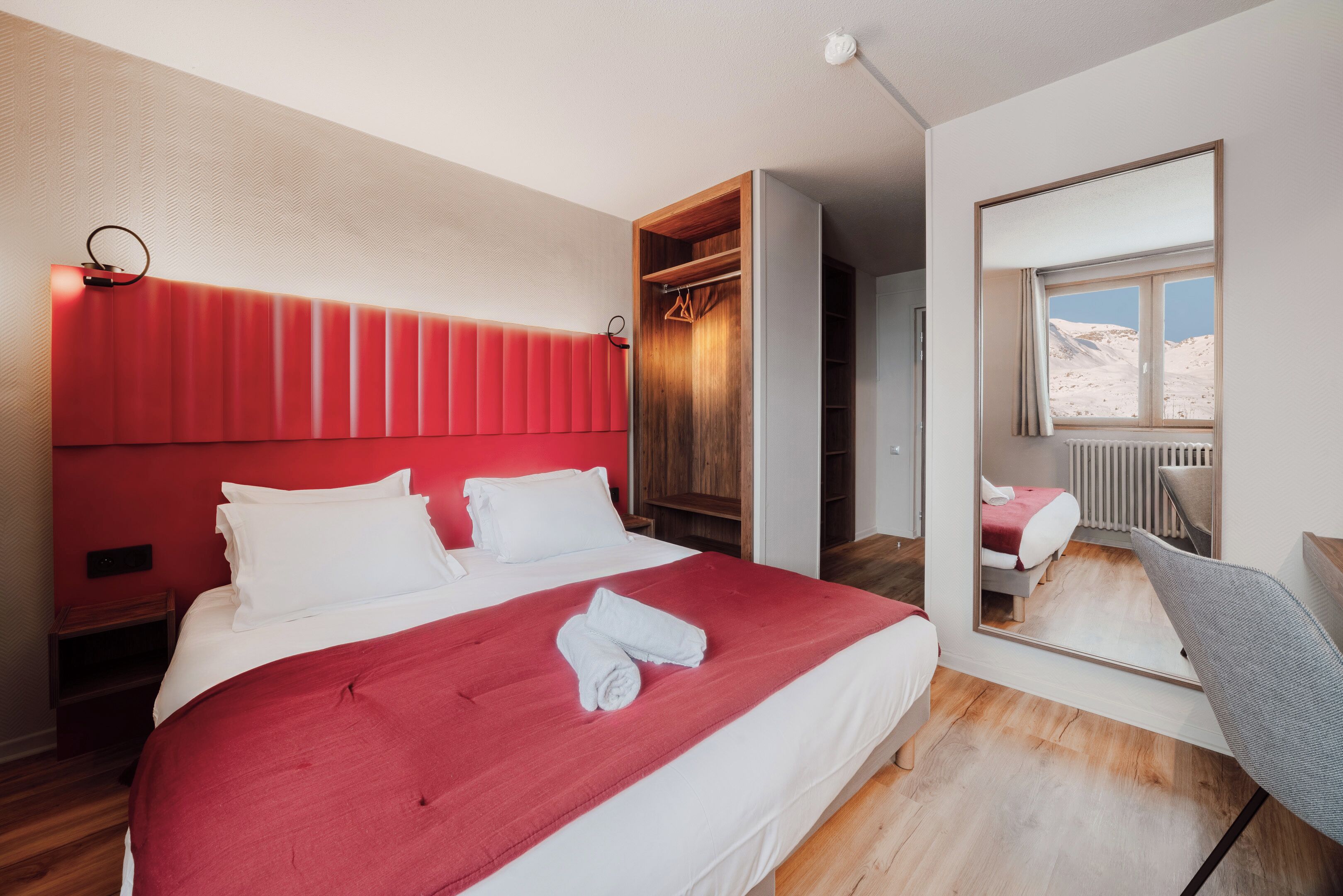 A modern hotel room with a large bed, a built-in wardrobe, a mirror, and a view of the outdoors.