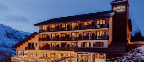 A multi-story hotel with balconies, a ski lift, and a mountain backdrop.