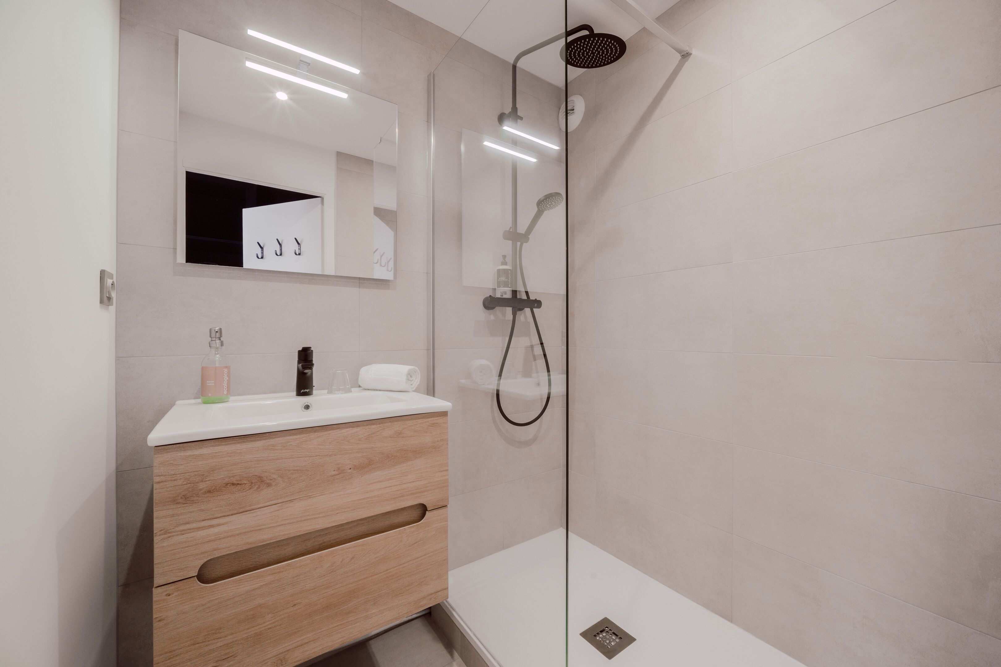A modern bathroom with a glass-enclosed shower, a wooden vanity with a mirror, and a white countertop.