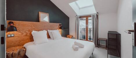 A modern hotel room with a large bed, wooden headboard, skylight, and a small side table.