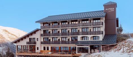Un hotel de varios pisos con balcones, un telesilla y el paisaje de una montaña.