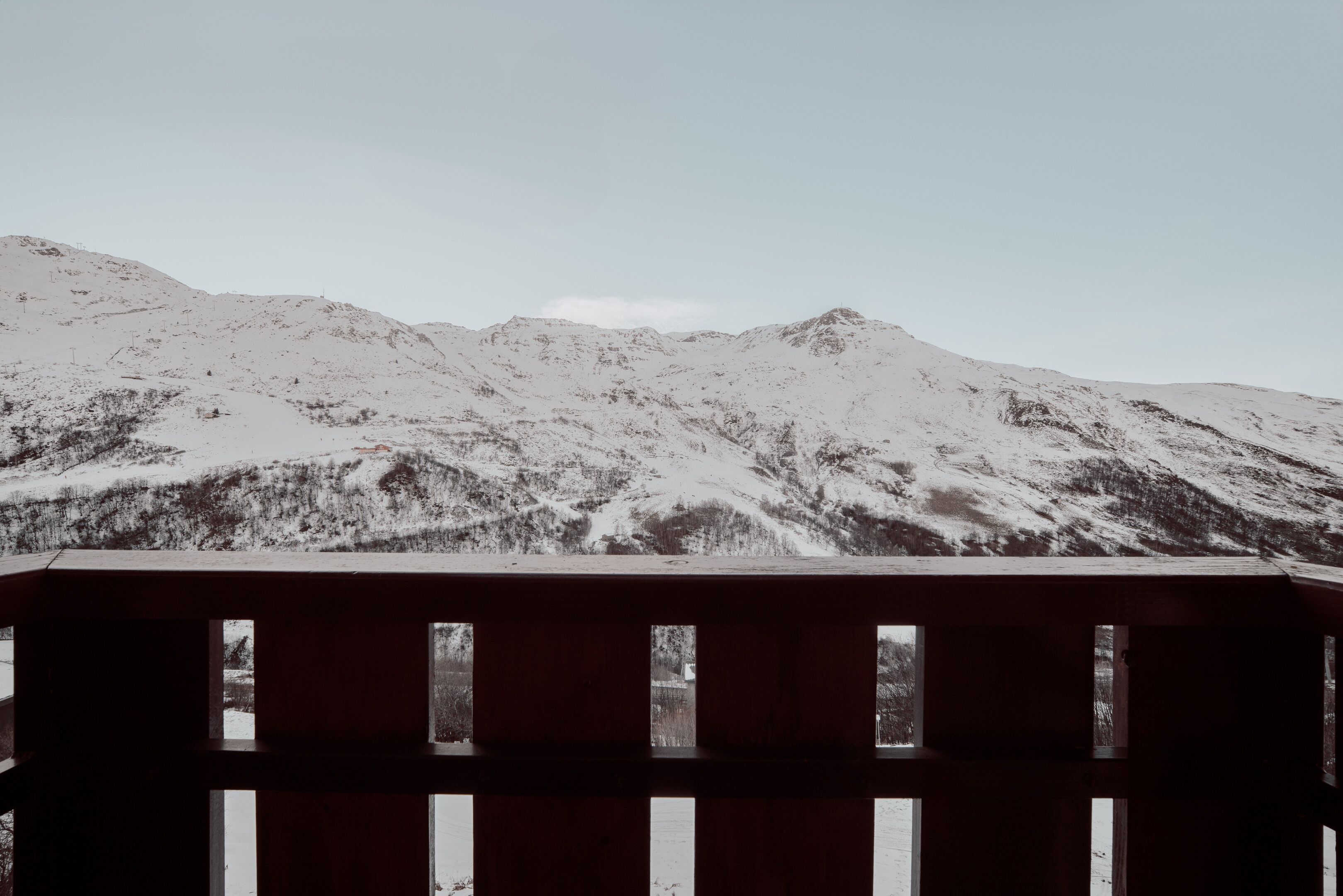 A view of snow-covered mountains through a wooden railing.