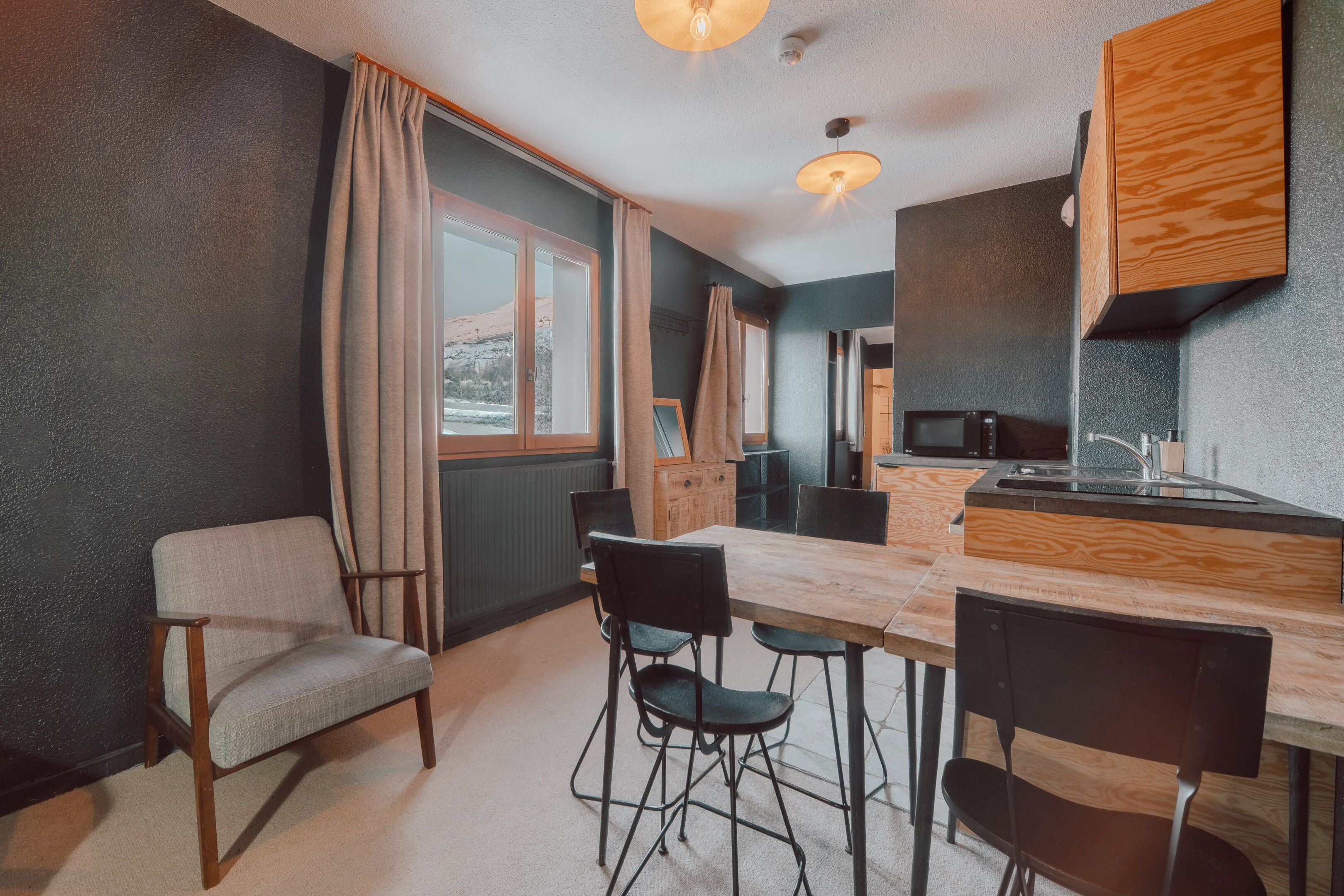 Cocina compacta con encimera de madera, comedor con sillas y vistas al exterior.