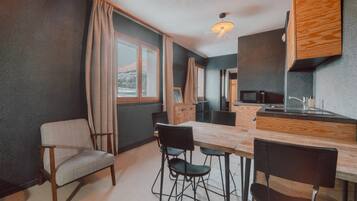 Cocina compacta con encimera de madera, comedor con sillas y vistas al exterior.