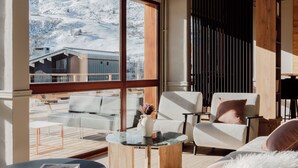 A modern living room with a large window, wooden furniture, and a view of a snowy mountain. - Alpeen Hotel (Les Belleville)