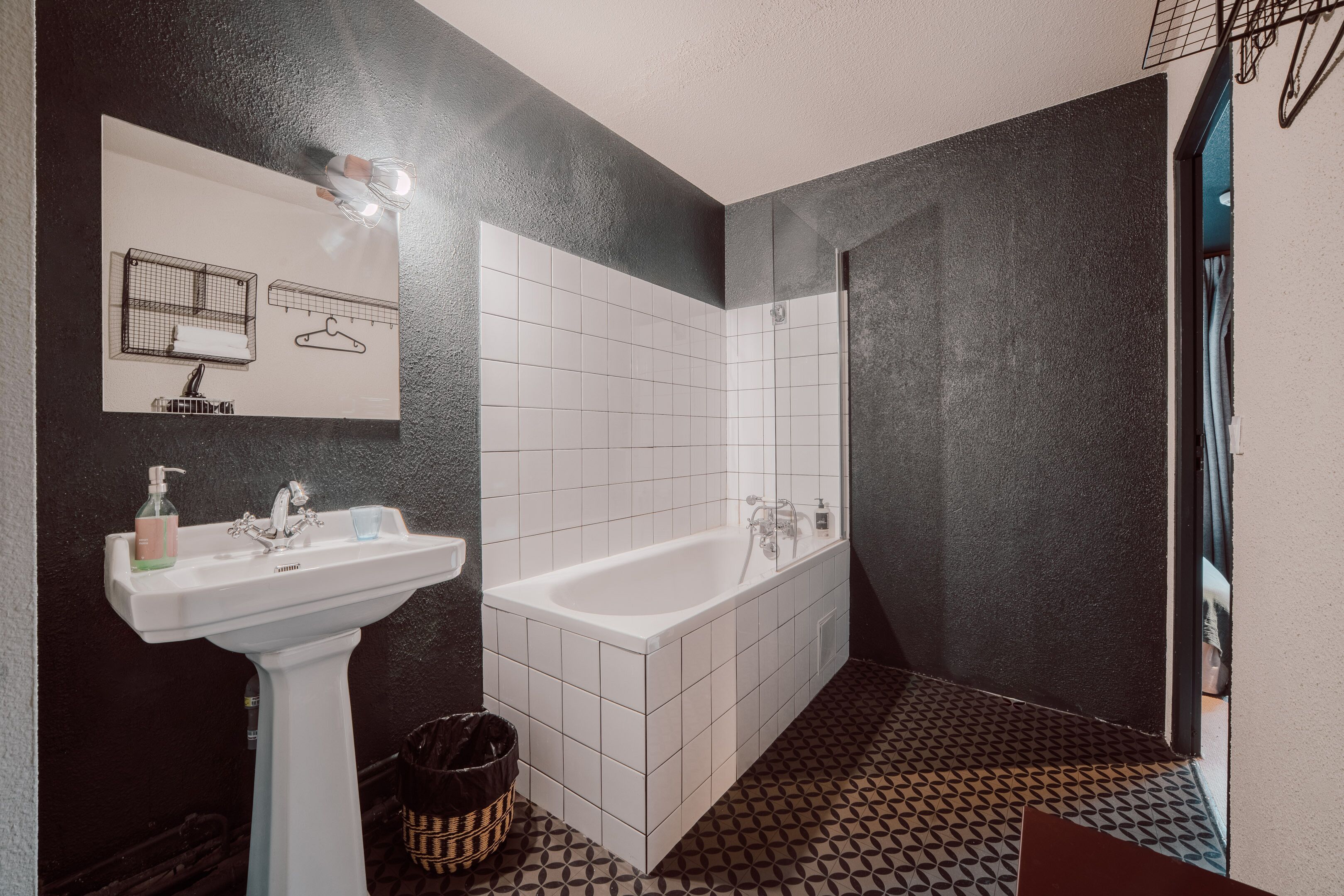 Ein Badezimmer mit einem weißen Waschbecken, einer Badewanne und einem Spiegel mit Gittermuster.