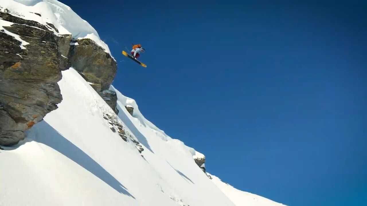 Un snowboarder realiza un salto desde un risco cubierto de nieve.