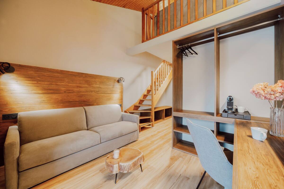 A modern living room with a wooden staircase, a sofa, a coffee table, and a dining area with a wooden table and chairs.