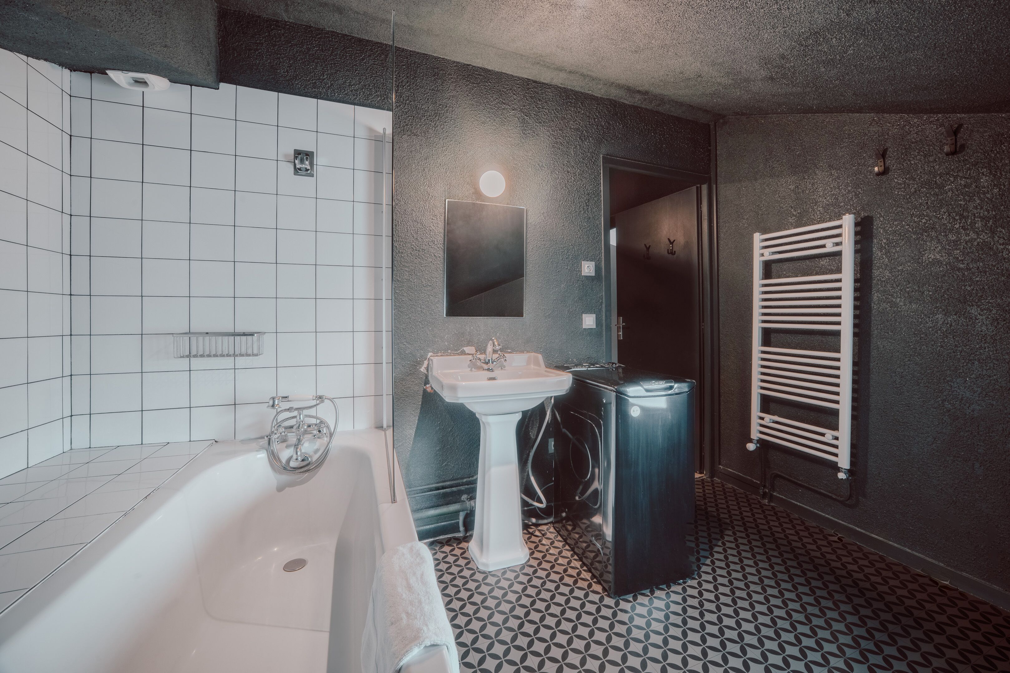 Un baño con una bañera blanca, un lavamanos pedestal, un espejo y un perchero para toallas.