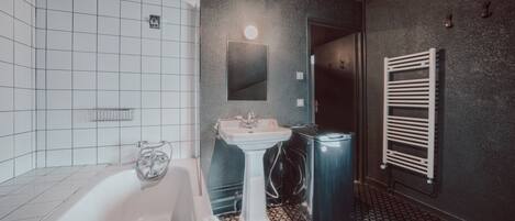 Un baño con una bañera blanca, un lavamanos pedestal, un espejo y un perchero para toallas.
