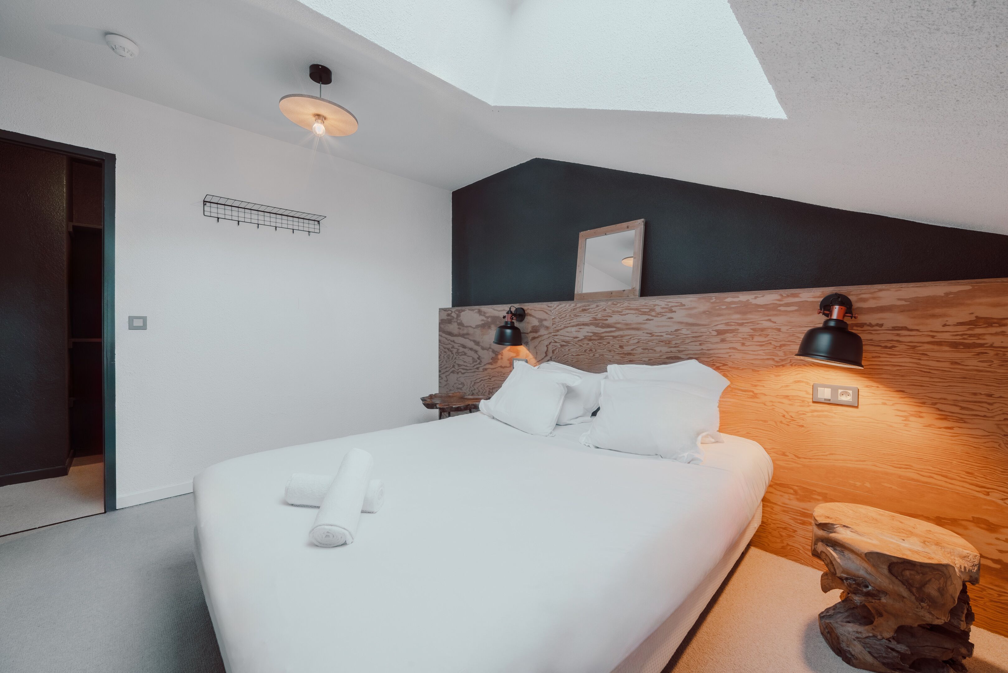 Une chambre à coucher moderne avec un grand lit, une lucarne, une tête de lit en bois et une table de chevet avec une lampe.