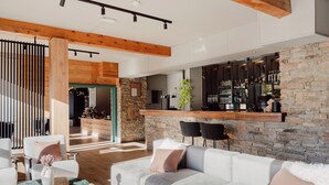 A modern living room with a large sofa, a coffee table, and a bar area with shelves of bottles. - Alpeen Hotel (Les Belleville)
