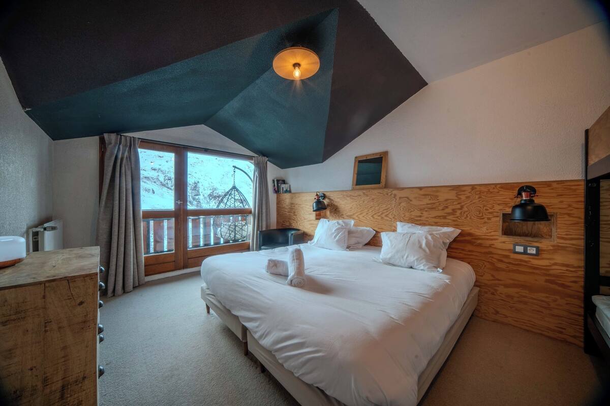 A bedroom with a large bed, wooden headboard, and a view of the outdoors through a window.