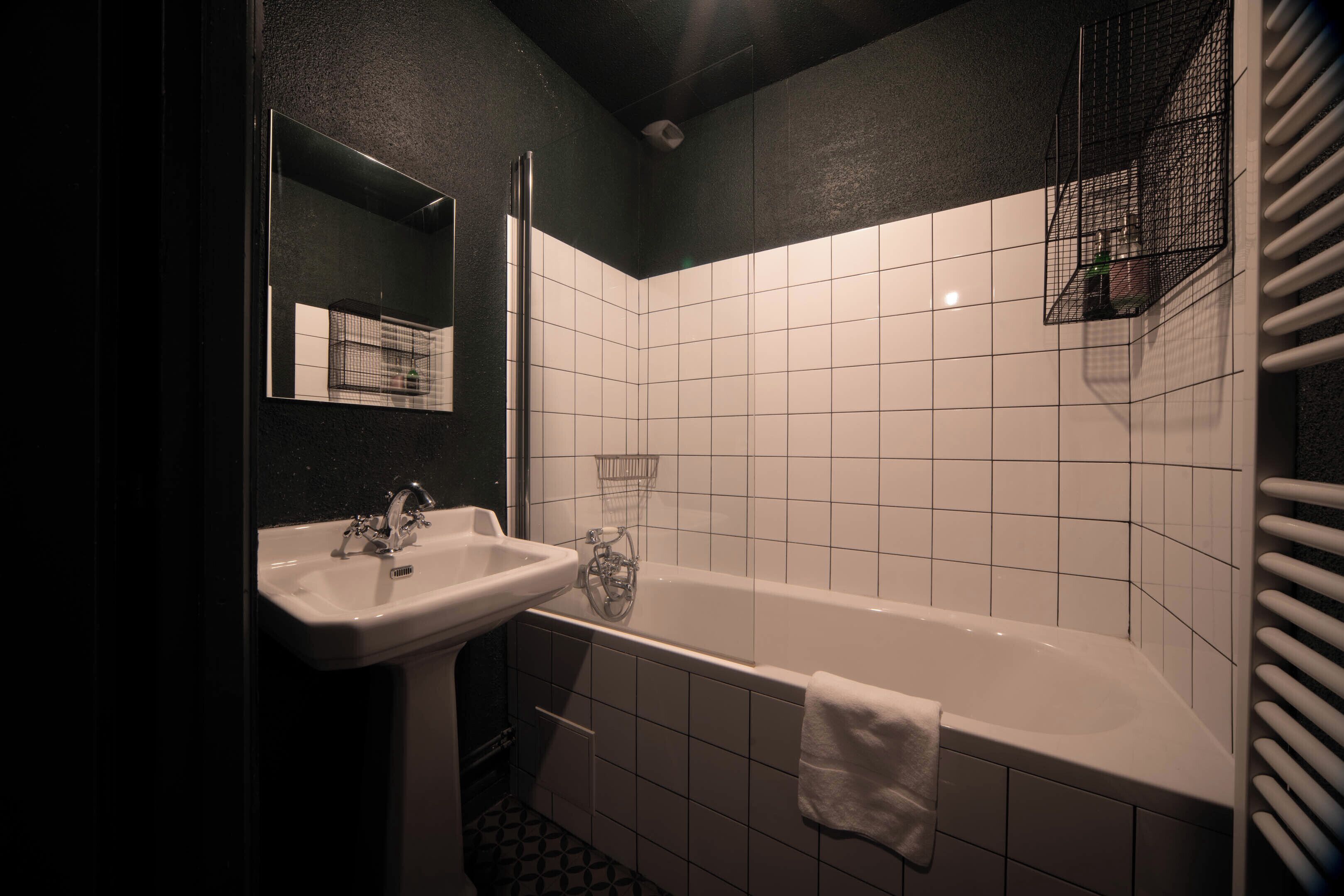 A bathroom with a white sink, a mirror, a bathtub, and a towel hanging on the wall.