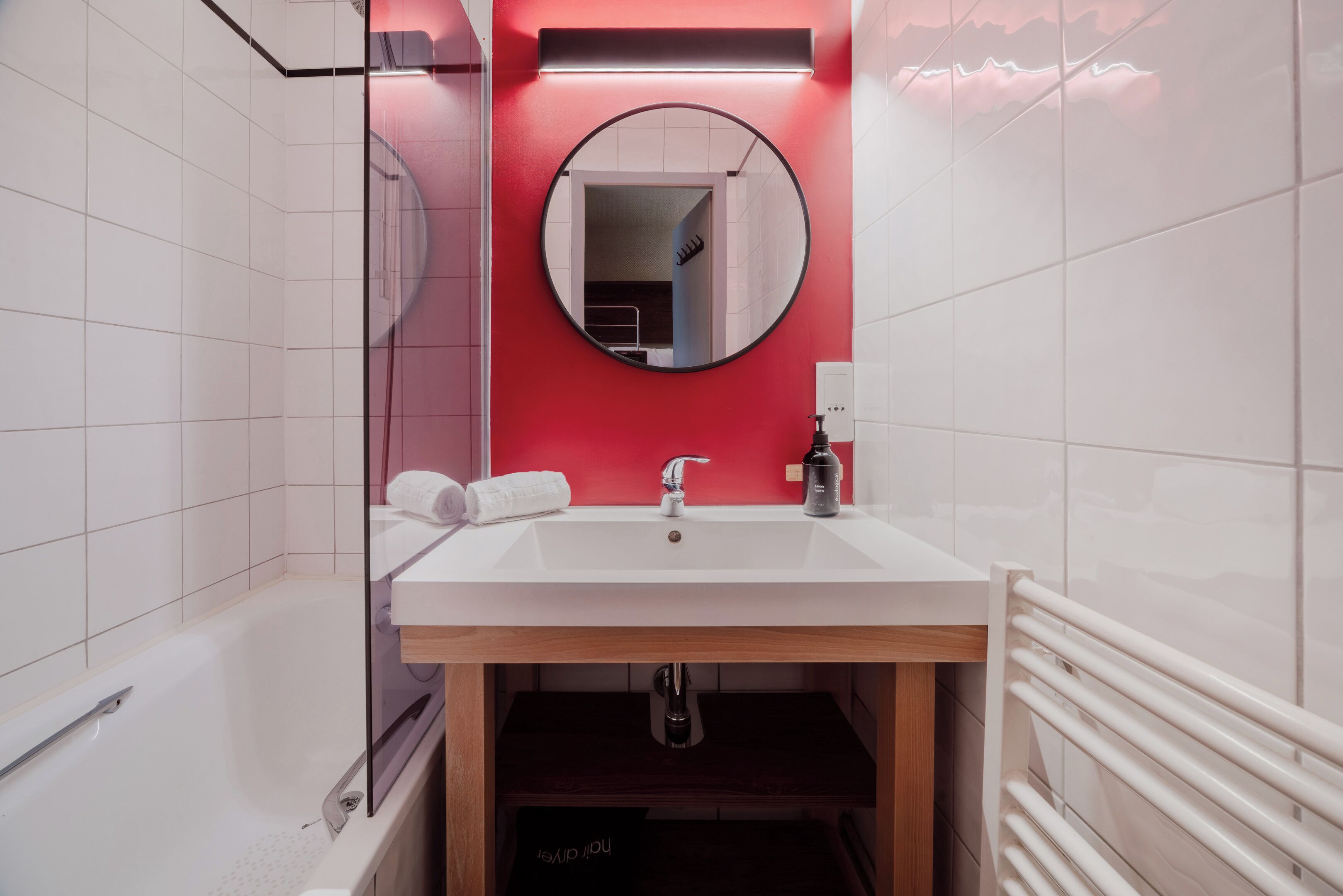 Ein Badezimmer mit einem weißen Waschbecken, einem Spiegel und einer roten Akzentwand.