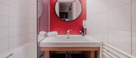 A bathroom with a white sink, a mirror, and a red accent wall.