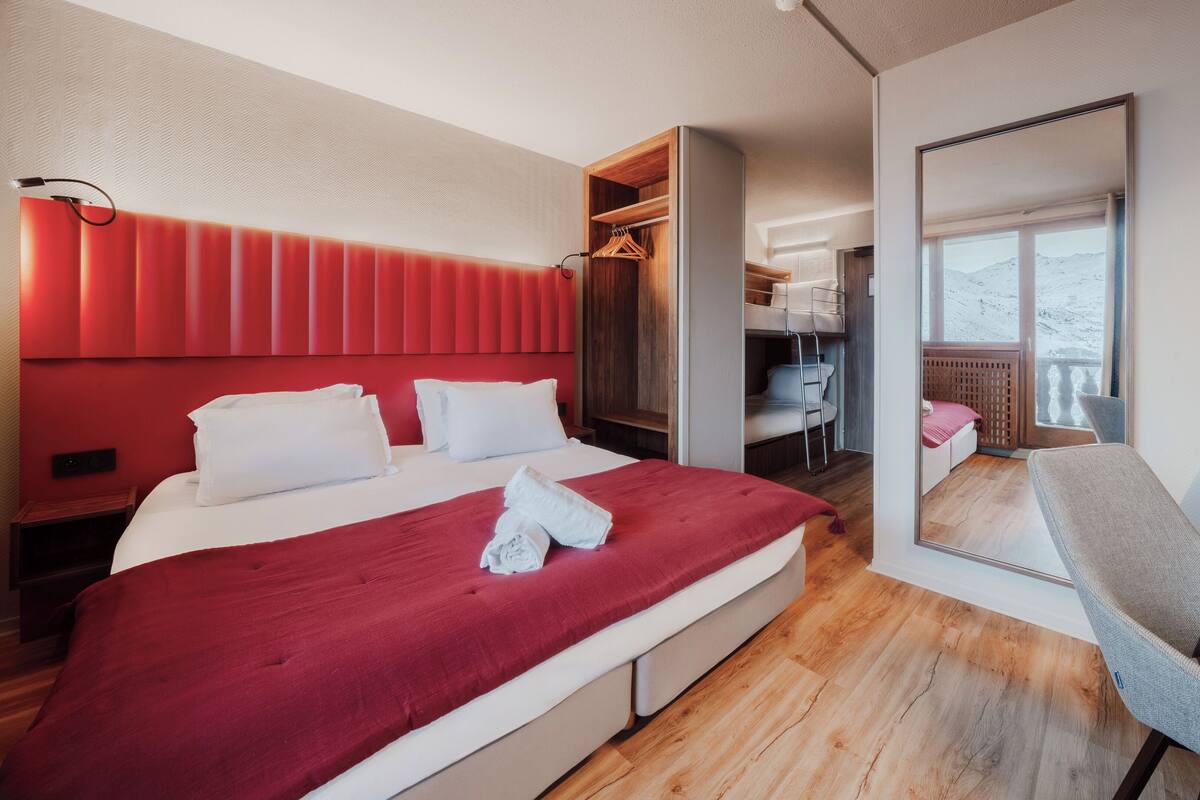 A modern hotel room with a large bed, a wooden wardrobe, a desk, and a chair.